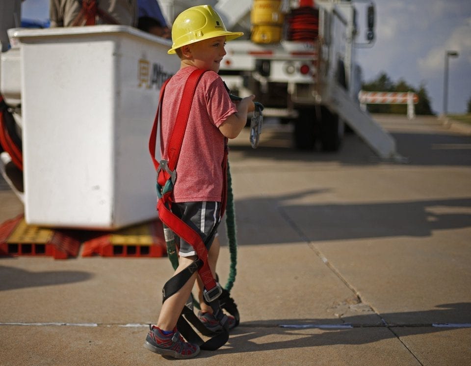 Young boy in a hard hat and safety harness in front of a Midwest Signs bucket truck